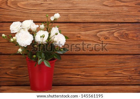White roses in a red bucket on a wooden background