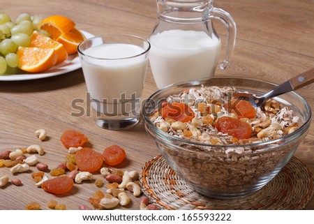Flakes with raisins, nuts and dried apricots and milk. Fresh fruit in the background