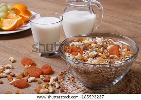 Cereal with raisins, nuts and dried apricots and milk. Fresh fruit in the background