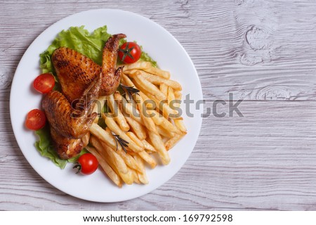 Two fried chicken wings, french fries, tomato and lettuce on a plate. top view