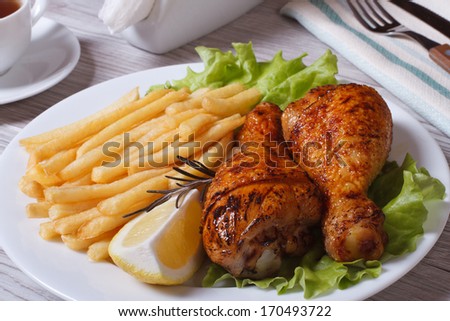 Two fried chicken drumsticks with french fries, rosemary and lemon on a white plate