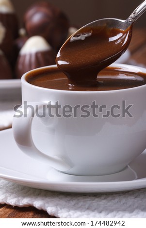 Chocolate dripping from a spoon in a cup closeup on background sweets on the table. vertical