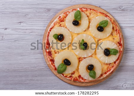 Pizza with pineapple rings, olives and basil on the table. top view