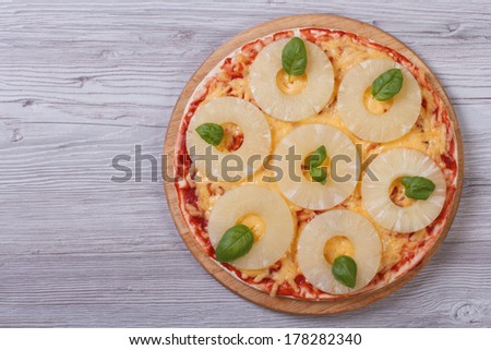 Pizza with pineapple rings and basil on the table. top view