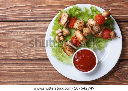 two fried chicken meat with vegetables on wooden skewers on a plate sauce. top view
