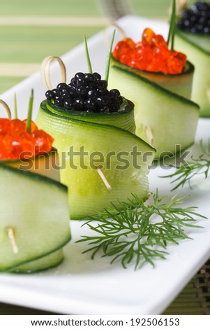 cucumber rolls with salmon red and black sturgeon caviar on a white plate closeup