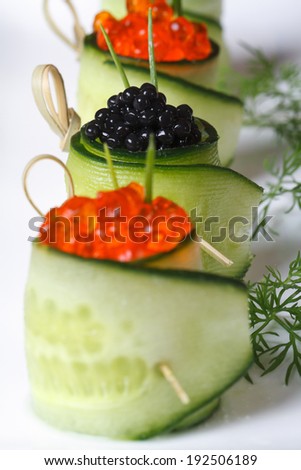Appetizer of cucumber rolls with red and black caviar on a white plate. macro vertical