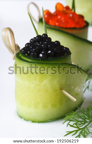 two cucumber rolls with red and black caviar on a white plate. macro vertical