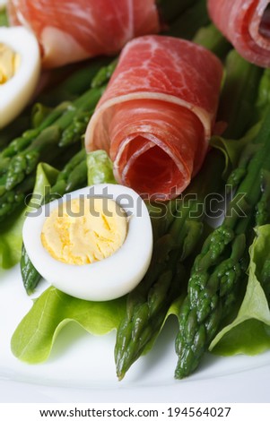 Asparagus with boiled eggs and ham on a white plate macro. vertical