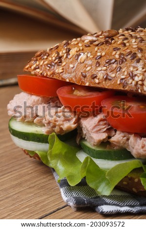 Tasty school lunch: a sandwich with tuna and vegetables macro on background of books on the table vertical