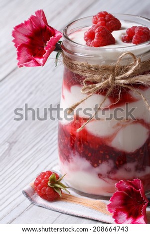 delicious raspberry yogurt in a glass jar closeup decorated with flowers on a wooden table. vertical