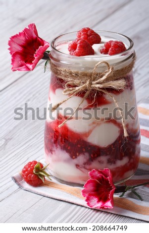 Milk dessert with raspberries in a glass jar closeup decorated with flowers on a wooden table. vertical