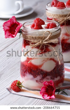 fresh raspberry yogurt in a glass jar closeup on a table decorated with flowers. vertical