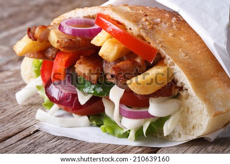 Doner kebab with meat, vegetables and fries in pita bread wrapped in paper close-up on the table horizontal