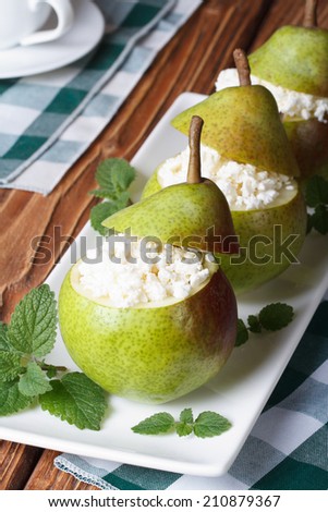 Fresh pears stuffed with cottage cheese on white plate closeup on table vertical