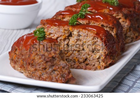 sliced meatloaf with ketchup and parsley closeup on a white plate, horizontal