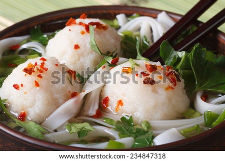 soup with fish balls, noodles and fresh herbs in a bowl and chopsticks macro. horizontal