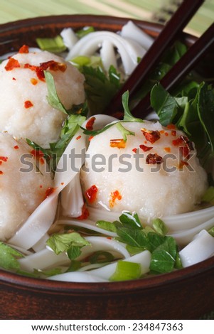 soup with fish balls, noodles and fresh herbs in a bowl and chopsticks macro. vertical
