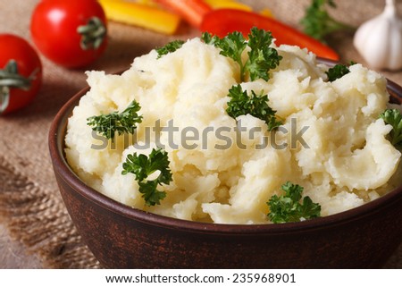 Delicious mashed potatoes with parsley in a bowl close-up on the table and vegetables. horizontal. rustic style