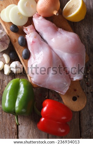 Raw meat rabbit legs on the kitchen blackboard and vegetables. close-up view from above vertical