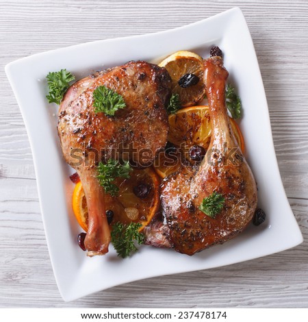 roasted duck leg with oranges and raisins on a white plate close up. top view
