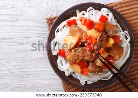pork meat in sweet and sour sauce with rice noodles close up on a plate. horizontal view from above