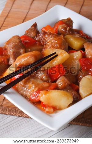 Asian pork meat with pineapple in sweet and sour sauce on a plate close-up. vertical