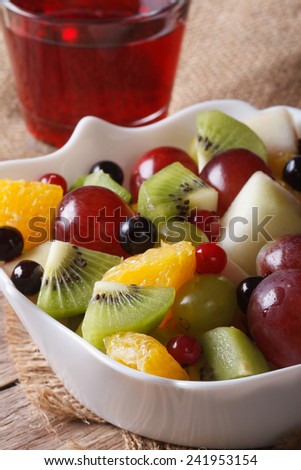 Fruit salad of oranges, grapes. pears, kiwis in a white bowl and grape juice closeup. Vertical