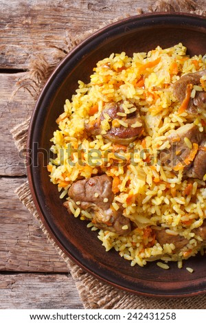 Rice with meat and vegetables on a brown plate closeup. Vertical view from above, rustic style