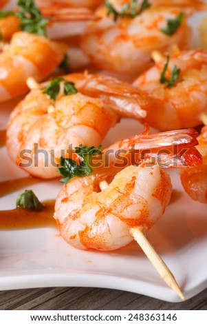 tasty grilled shrimp on wooden skewers macro on a plate. vertical