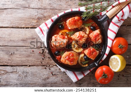 Fish in tomato sauce with olives and lemon in a frying pan. horizontal view from above