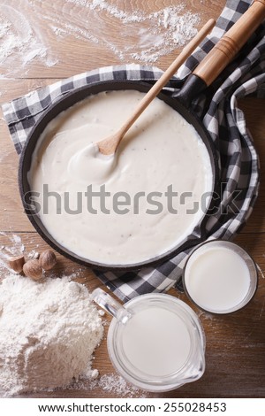 bechamel sauce in a pan and flour, milk on the table. vertical top view close-up