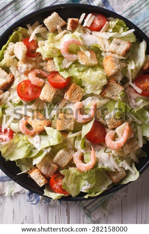 Fresh Caesar salad with shrimps closeup on a black plate. vertical top view