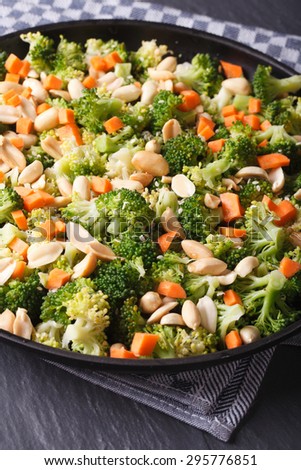 Broccoli with peanuts and carrots close-up on a black plate. vertical