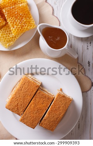 Sliced honey cake on a plate close-up, coffee, and a honeycomb. vertical top view