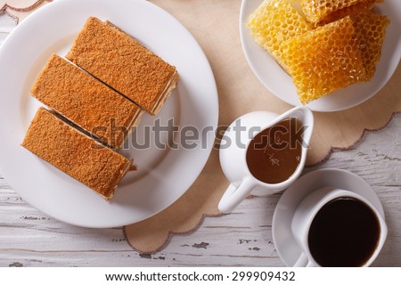Sliced honey cake on a plate close-up, coffee, and a honeycomb. Horizontal top view