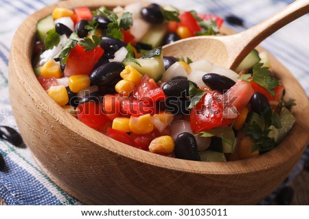Mexican vegetable salad with black beans, avocado and corn close up in a wooden plate. horizontal
