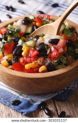 Mexican vegetable salad with black beans, avocado, corn and tomatoes closeup in a wooden plate. vertical
