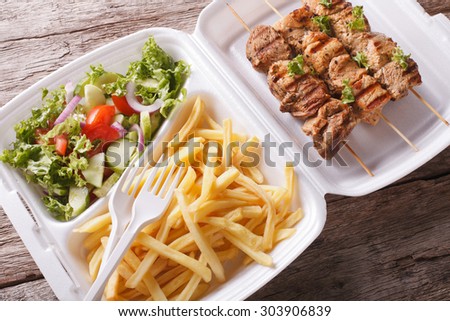 Lunch Box: kebabs, fries and fresh salad in tray close-up on the table. Horizontal