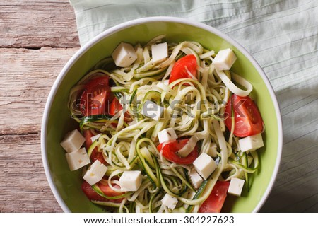 zucchini pasta with feta cheese and tomatoes close up in a bowl on the table. horizontal view from above