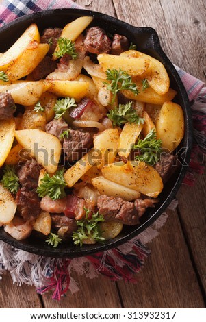 fried potatoes with meat and bacon served in a pan close-up. vertical view from above