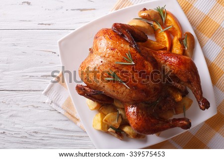 baked whole chicken with oranges and potatoes on a plate. horizontal view from above