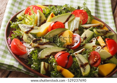 gourmet salad of mango, avocado, kiwi, lettuce, tomato dressed with balsamic sauce close-up on a plate on the table. horizontal