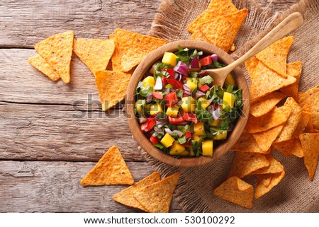 Delicious salsa with mango, chilli pepper, cilantro and onion close up in a bowl and nachos on the table. horizontal view from above