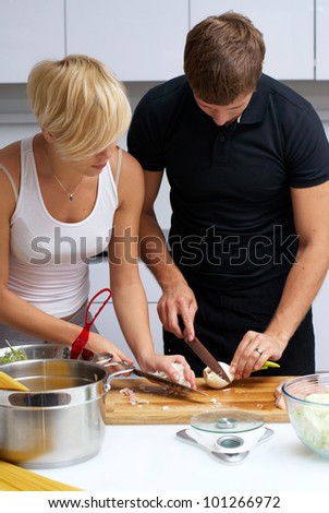 Playful young couple in their kitchen making dinner. kitchen is white and filled with light. couple is young and fit
