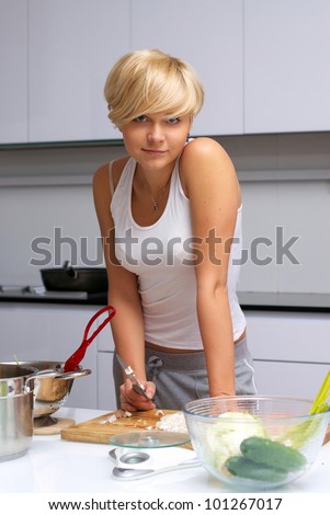 Portrait of pretty blond girl in the kitchen making pasta. kitchen is white and filled with light. lady is young and fit