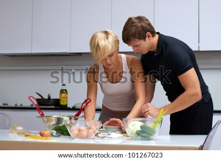 Playful young couple in their kitchen making dinner. kitchen is white and filled with light. couple is young and fit.