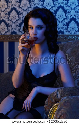 Retro pin-up girl wearing vintage lingerie in luxury interior with glass of whiskey in her hand