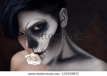 Young woman in day of the dead mask skull face art and rose in her mouth