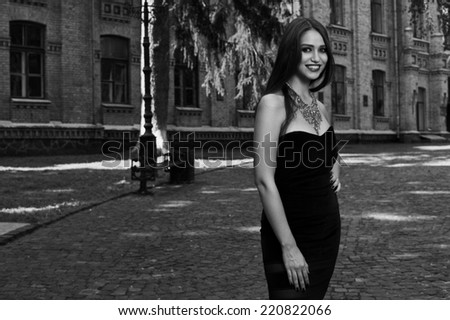 sexy woman in black dress and necklace near old building  black and white photo